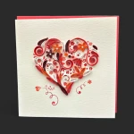 Gros plan sur une carte saint valentin geneve artisanale : un cœur en quilling coloré rouge et orange avec le mot 'love'.