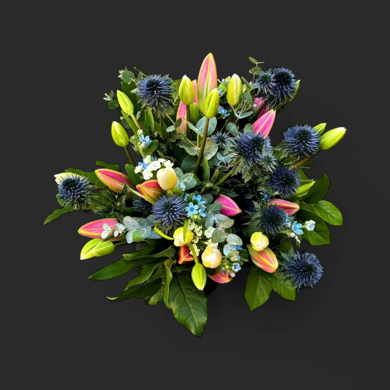 Gros plan du bouquet lis roses chardons genève, avec ses boutons de lis roses délicats, ses chardons d'un bleu profond et son feuillage d'eucalyptus.