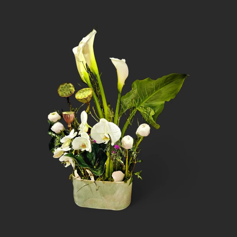 Élégante composition florale blanche geneve avec arums élancés, orchidées nacrées et capsules de lotus sur fond noir.