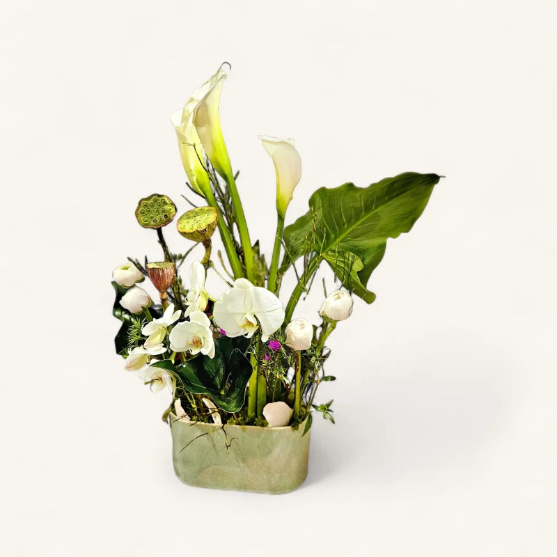 Élégante composition florale blanche genève avec arums, orchidées et pods de lotus sur fond noir, créée par votre fleuriste.